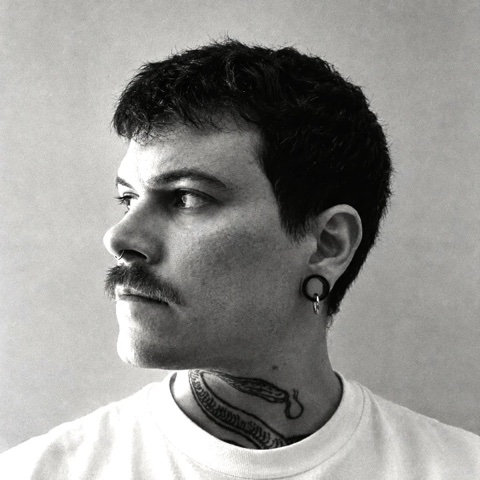 Portrait en noir et blanc d’Arthur, de profil, moustache, anneaux aux oreilles et serpent tatoué dans le cou